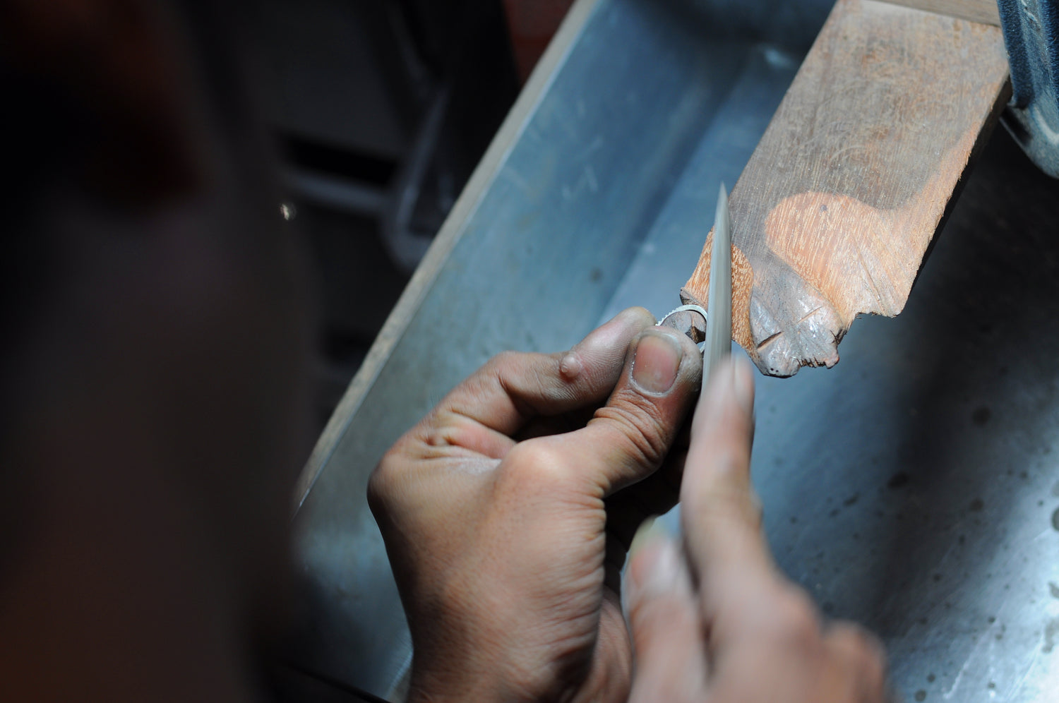 Jeweler’s hands carefully filing a sterling silver ring on a wooden bench pin during finishing process; แต่งตัวเรือน เก็บรายละเอียดด้วยมือที่เวิร์กช็อป Madduck Jewels
